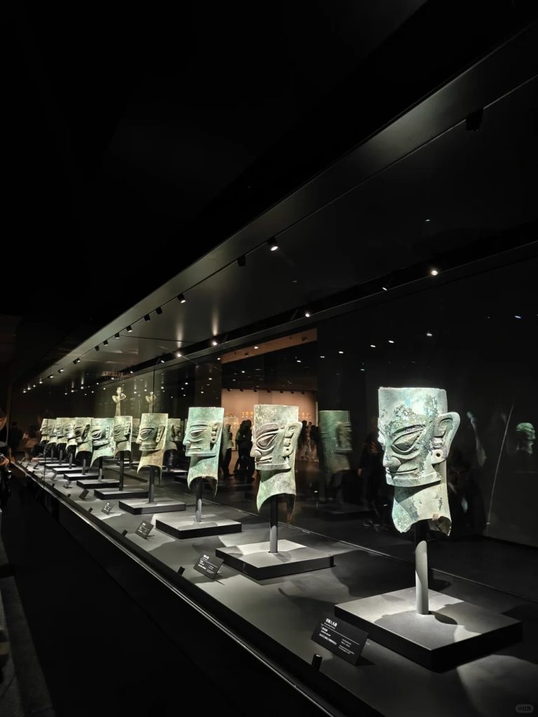 Display case of Sanxingdui bronze alien-style masks in museum lighting