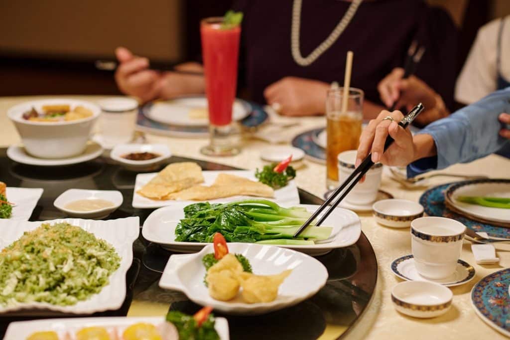 People sharing a Chinese family-style meal at a restaurant round table, assorted Cantonese dishes and tea