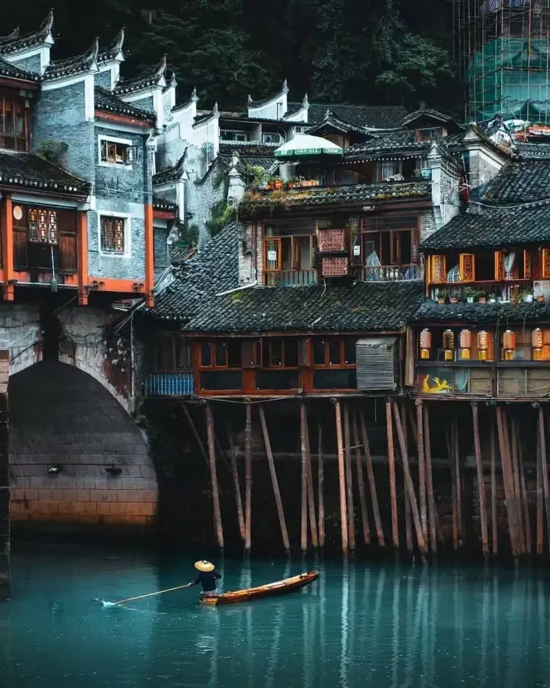 Timber stilt houses above the Tuo River in Fenghuang, with a small wooden boat below