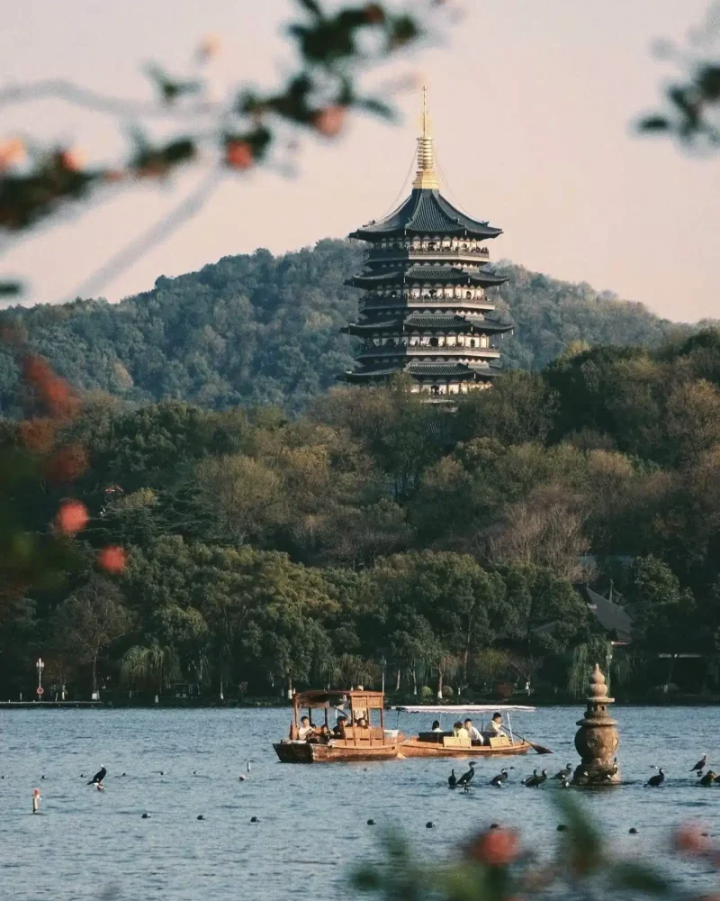 Leifeng Pagoda on a wooded hill above West Lake, with a sightseeing boat on the water