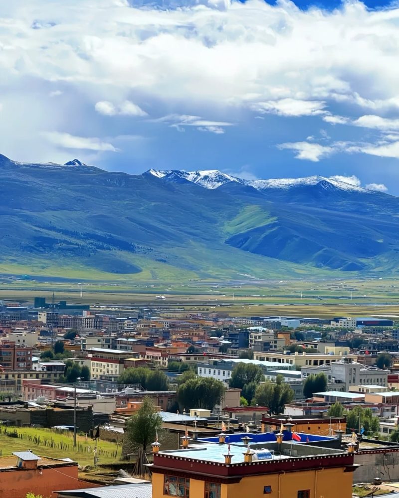Litang rooftops beside highland grasslands and distant snow-dusted mountains in Sichuan