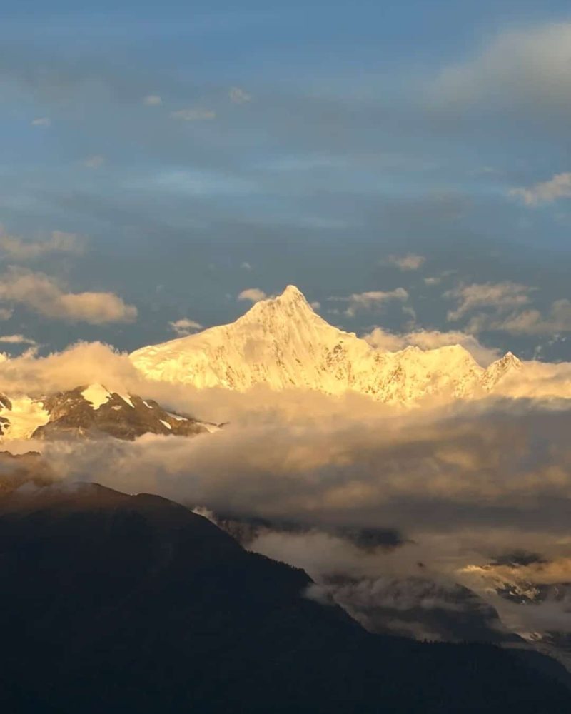 Golden morning light on a snow-covered Meili peak above drifting clouds near Deqin