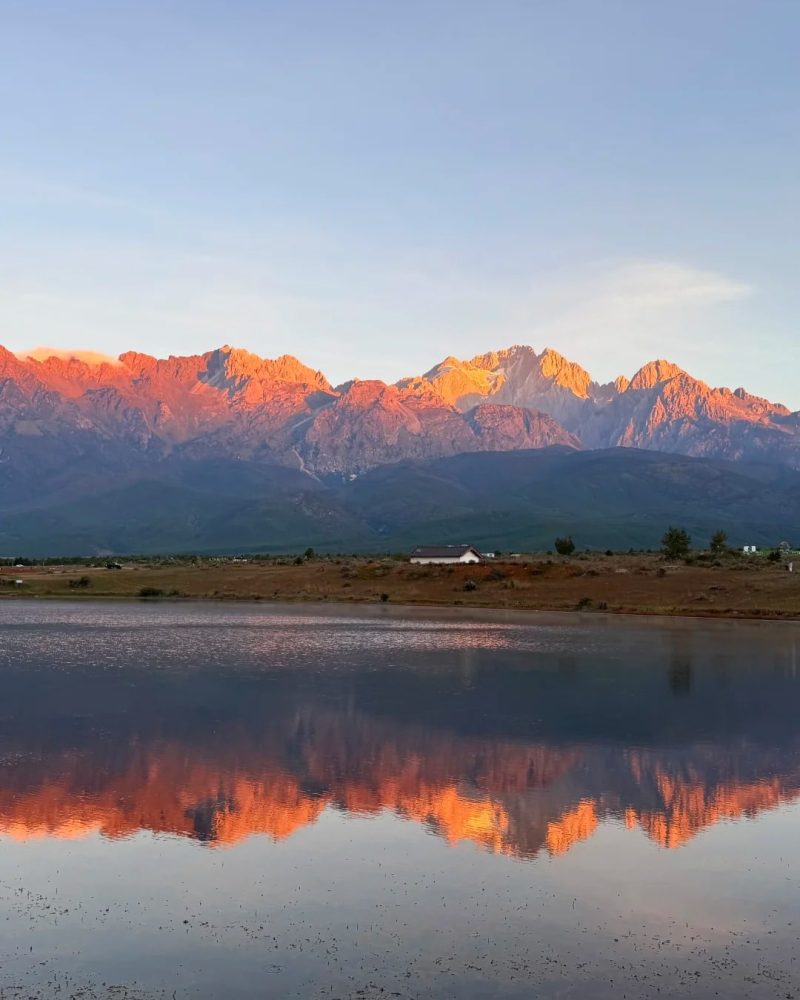 Golden-lit mountain peaks reflected in a still lake in the Meili Snow Mountain area of Yunnan