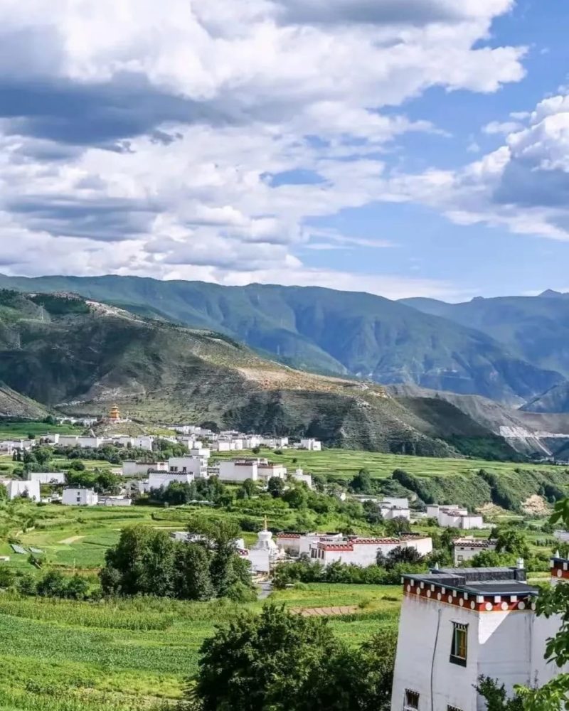 White Tibetan houses among green fields in a mountain valley in Xiangcheng, western Sichuan