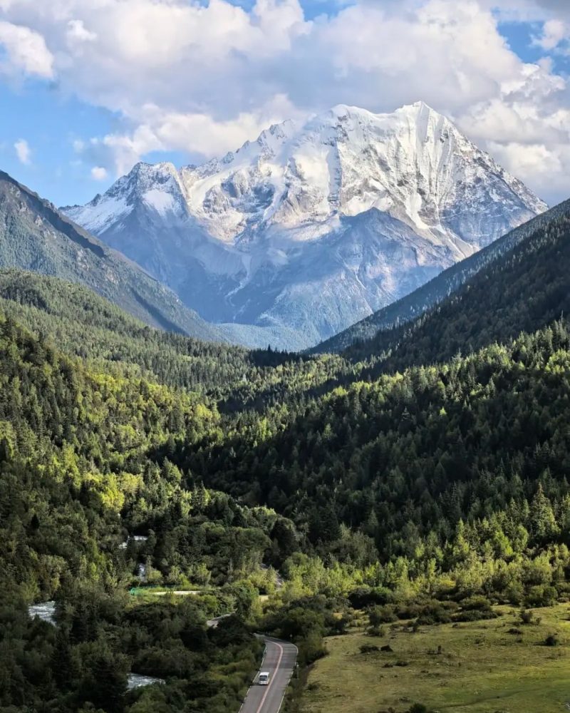 A winding road through a forested valley beneath snow-covered peaks near Xinduqiao, western Sichuan
