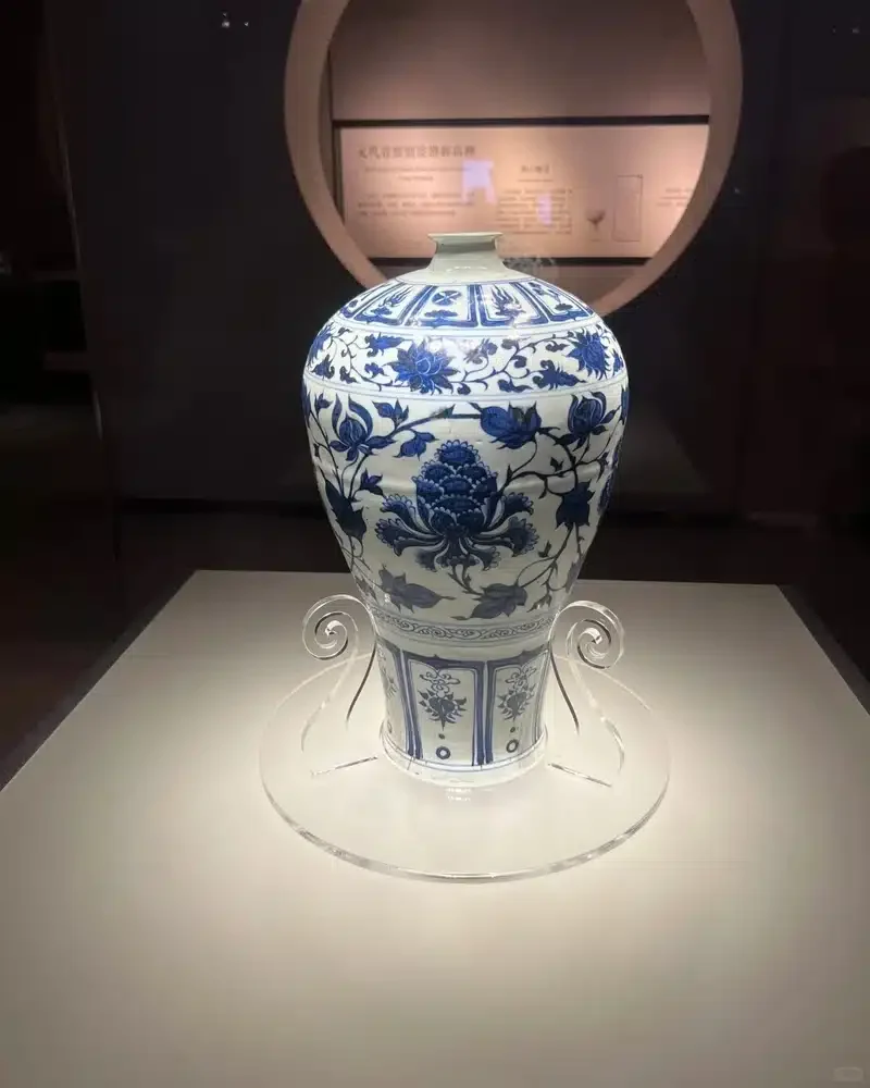 A blue-and-white porcelain vase with floral decoration on a transparent museum display stand.