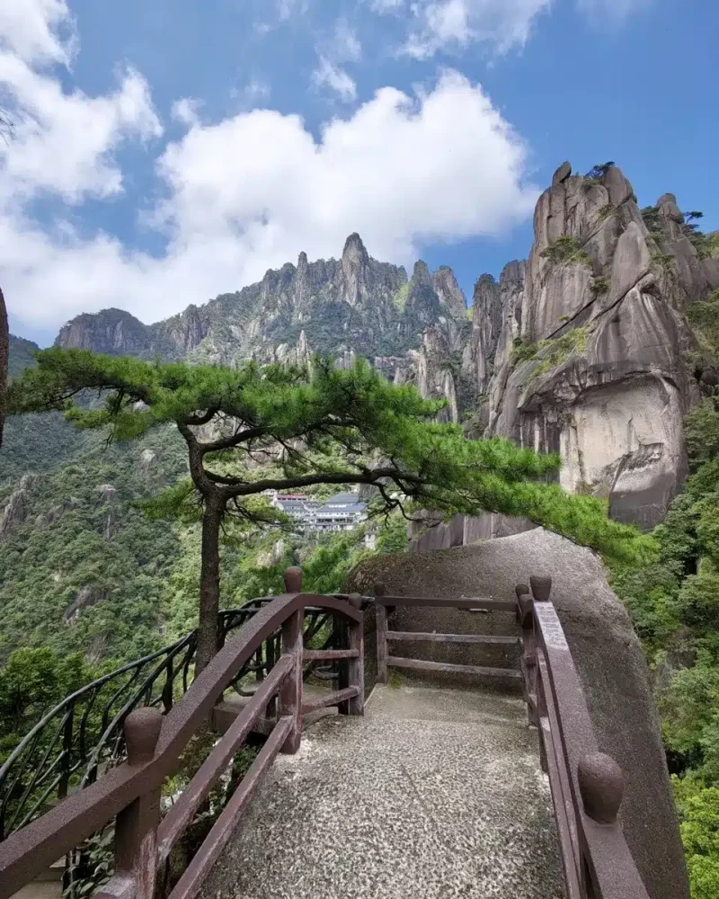 A pine tree and a railed stone walkway overlook granite peaks at Sanqingshan.