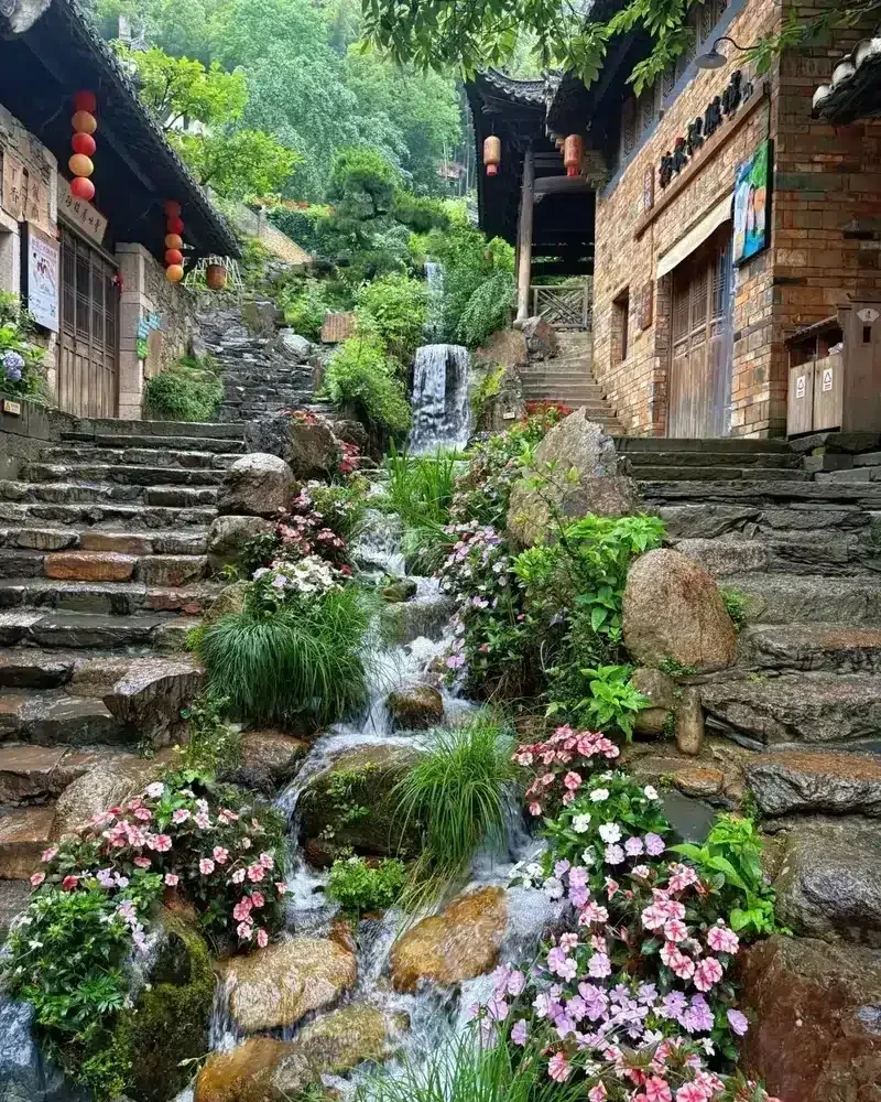 Flowers border a stepped stream between stone stairways and village buildings in Huangling.