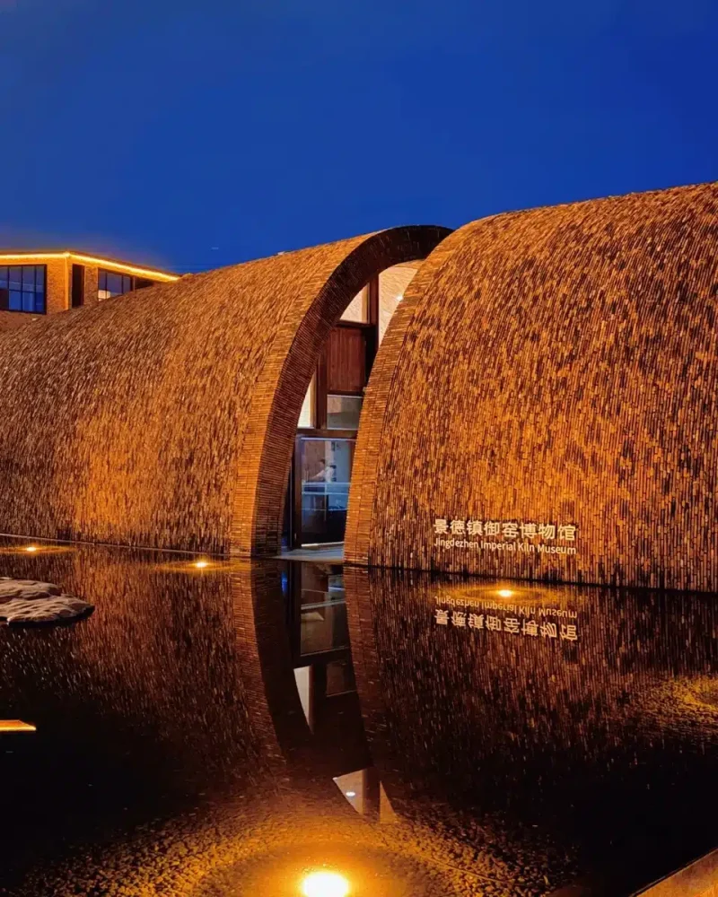 Illuminated brick vaults and the museum sign reflect in water at Jingdezhen Imperial Kiln Museum beneath a deep blue sky.
