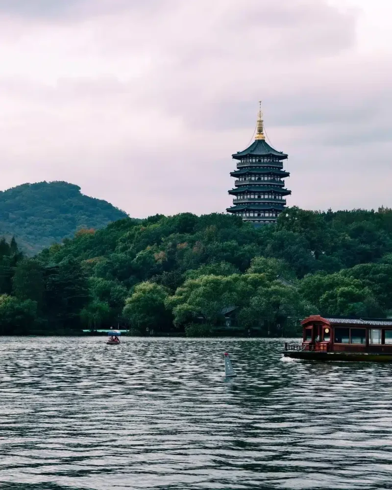 A small boat crosses West Lake with wooded hills and Leifeng Pagoda in the background in Hangzhou.