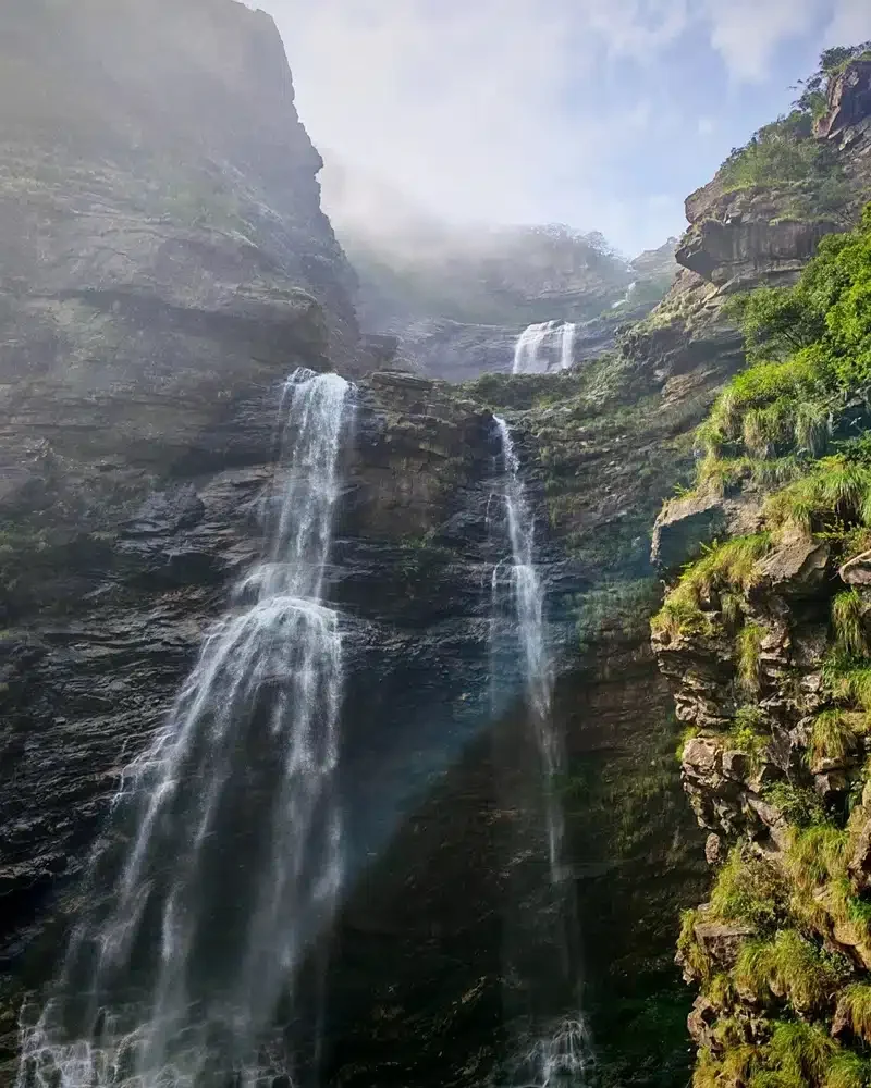 Sandiequan Waterfall flows over layered rock between high cliffs, with mist above the upper cascade at Lushan.