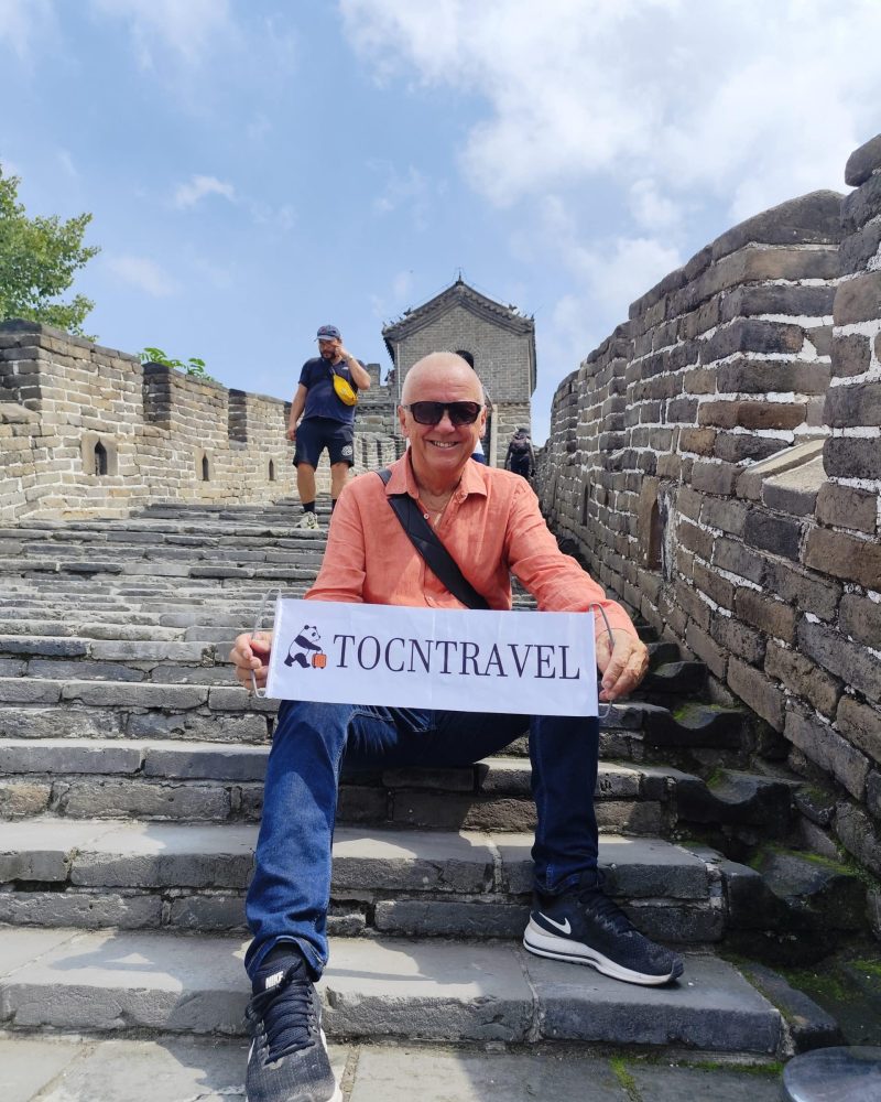 A TOCNTRAVEL guest holding a sign while sitting on the Great Wall in Beijing.