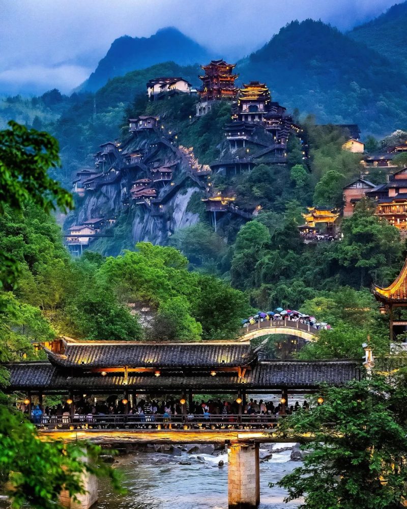 Wangxiangu cliffside village in Jiangxi, China, lit up at night above a river valley