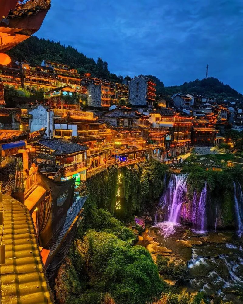 Night view of Furong Town in Hunan, China, with illuminated old buildings and a waterfall