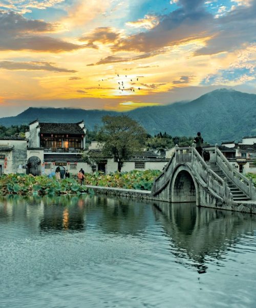 Traditional Huizhou stone arch bridge with sunset sky and lotus pond