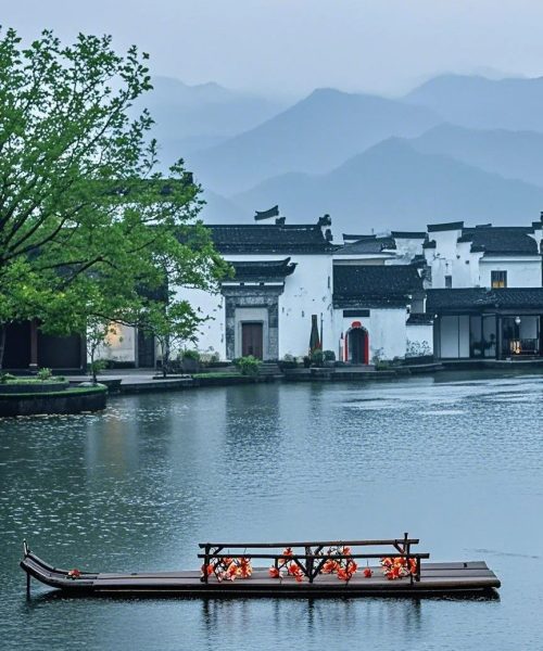 Huizhou riverside village with traditional white houses and misty mountain background