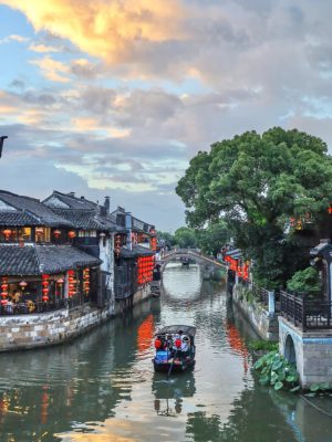 Traditional wooden boat cruising under arched bridges in a historic Jiangnan water town near Hangzhou.