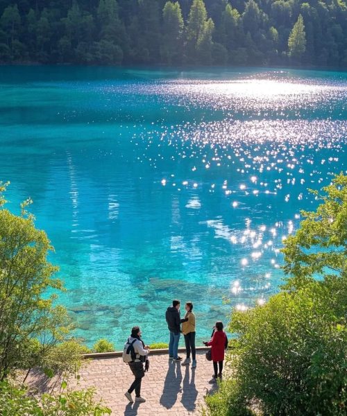"Tourists admiring the crystal-clear blue lake and reflections in Jiuzhaigou Valley"