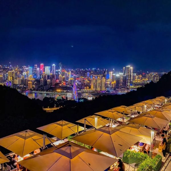 Dining under umbrellas at Nanshan Yikeshu with panoramic night view of Chongqing’s illuminated skyline.