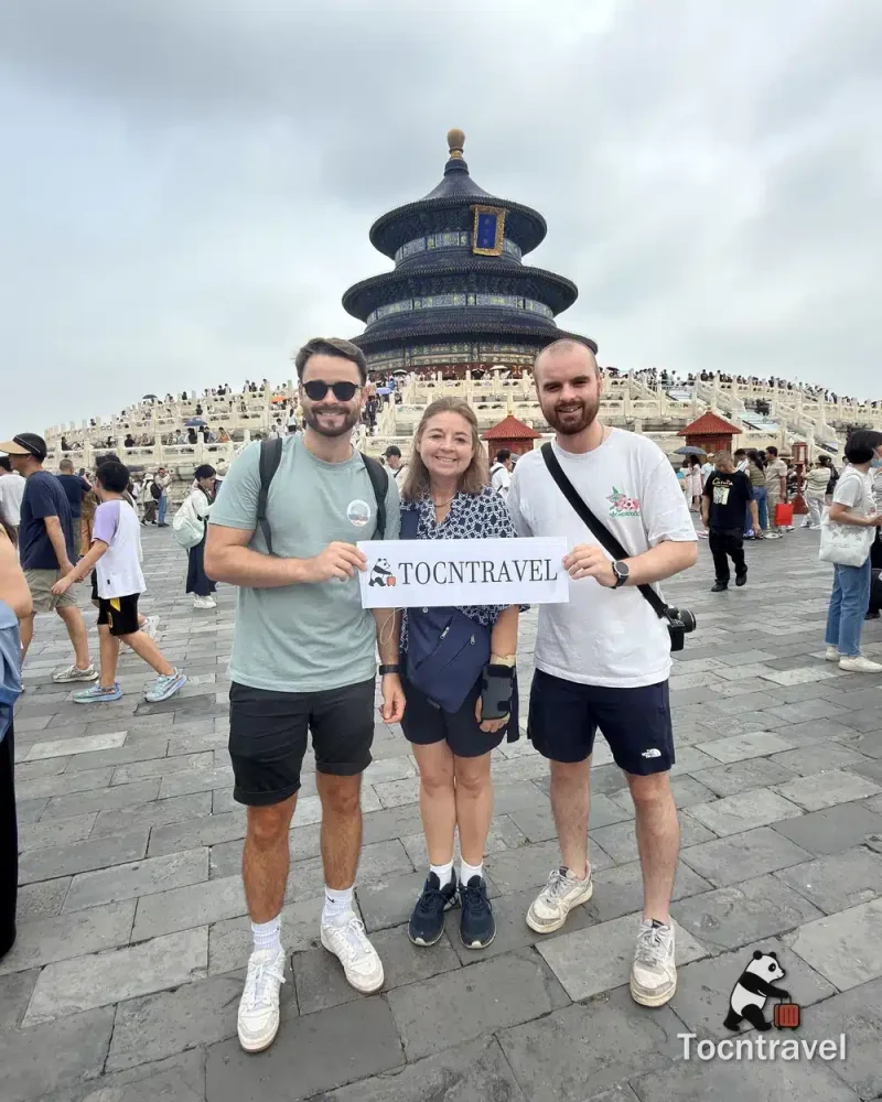 Three TOCNTRAVEL guests holding a sign in front of the Hall of Prayer for Good Harvests in Beijing
