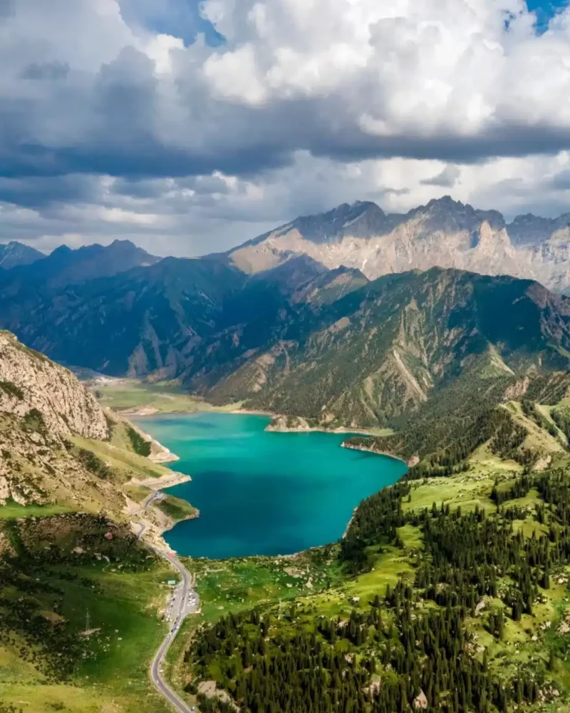 Turquoise alpine lake surrounded by steep mountains and conifer forest along the Duku Highway in Xinjiang.