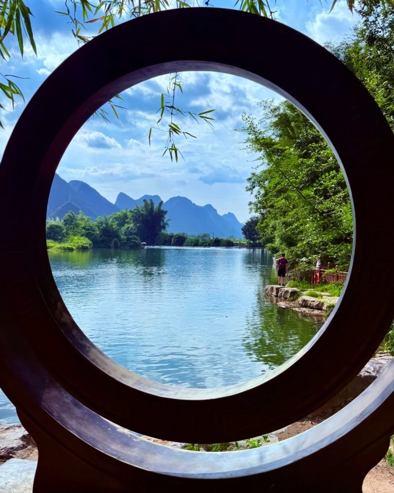 Karst landscape in Yangshuo, China, with lake views framed by a circular window and green mountains beyond